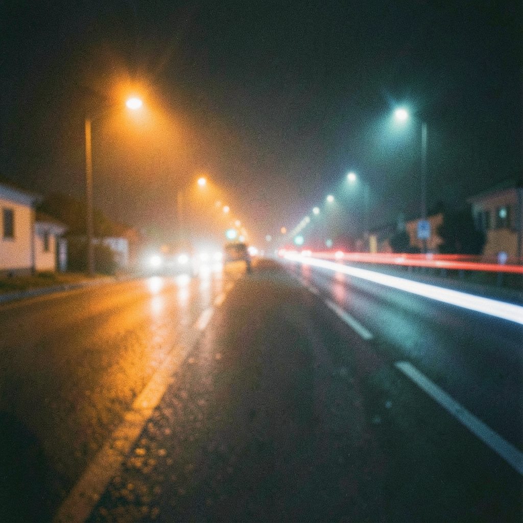 Verschwommene nächtliche Straße mit Lichtspuren von Fahrzeugscheinwerfern, warme orange und kühle blaue Töne, körniges analoges Filmbild